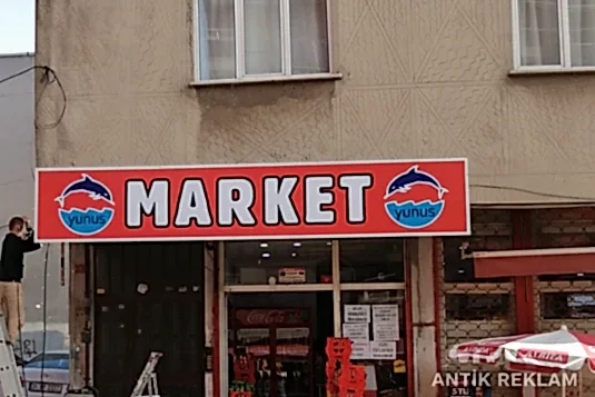 Market vinil baskılı cephe tabelası kırmızı zemin beyaz yazı yunuslu logo dış mekan uygulaması