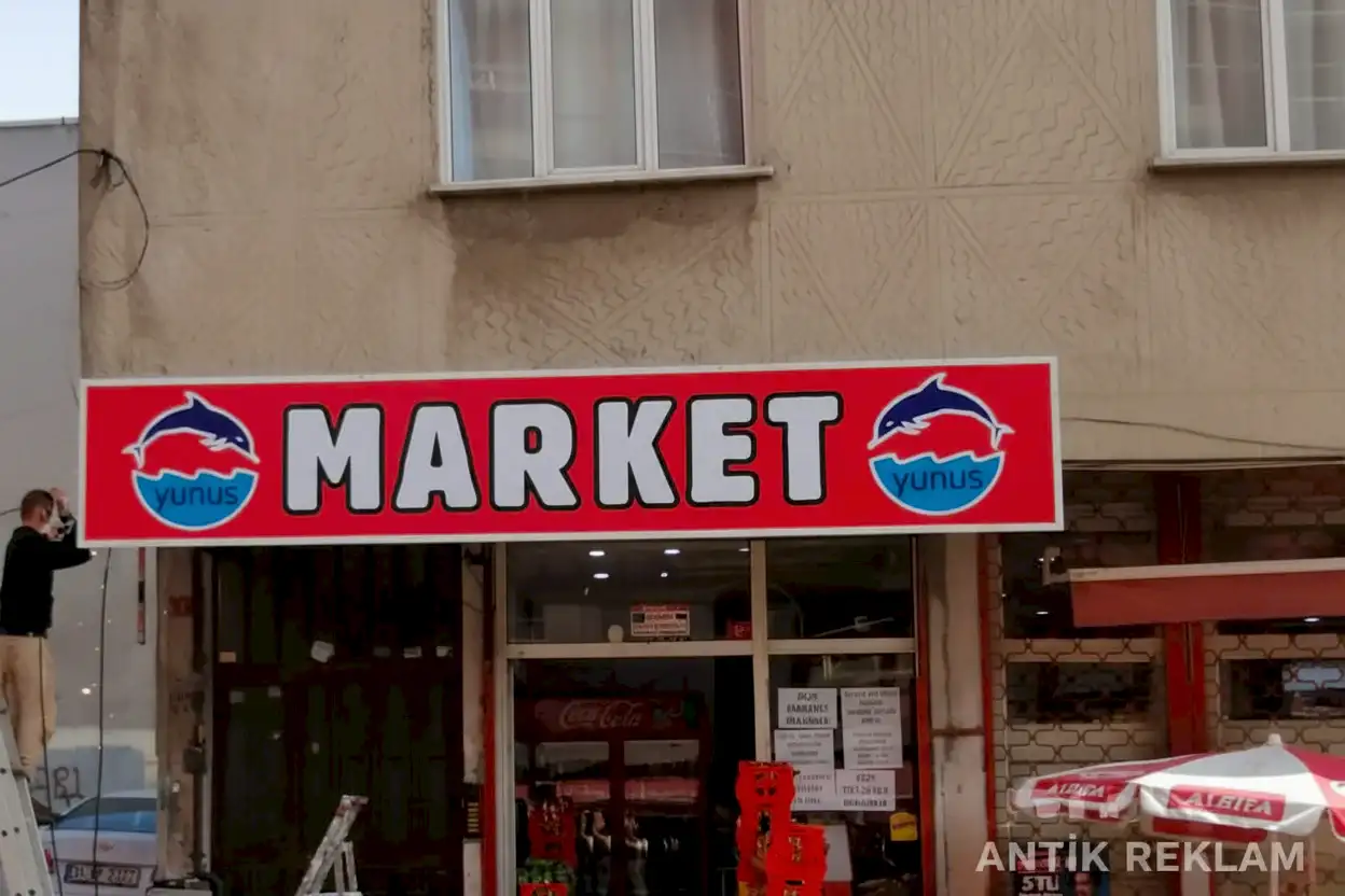 Market vinil baskılı cephe tabelası kırmızı zemin beyaz yazı yunuslu logo dış mekan uygulaması